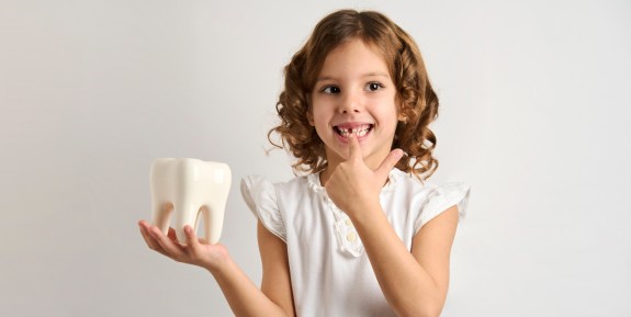 Kleines Mädchen zeigt stolz auf ihre Zahnlücke und hält ein übergroßes Zahnmodell