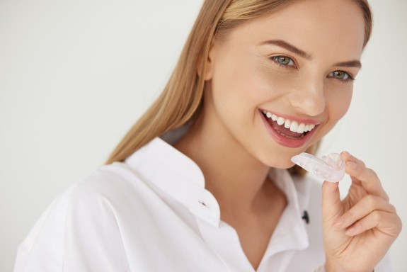 Junge Frau lacht und hält eine Zahnschiene in der Hand